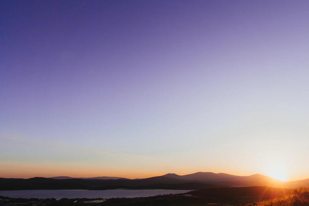 silhouette of mountains near body of water during orange sunset