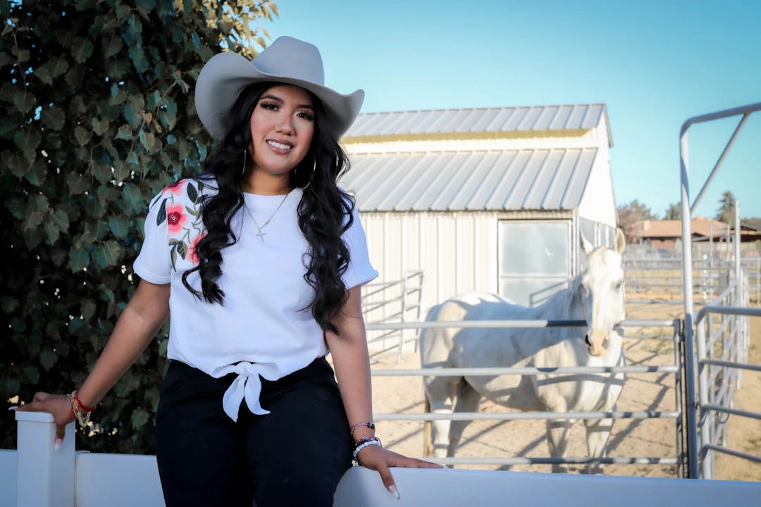 a woman in a cowboy hat sitting on a fence